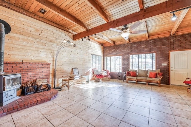 living room featuring ceiling fan, a wood stove, brick wall, and light tile patterned flooring