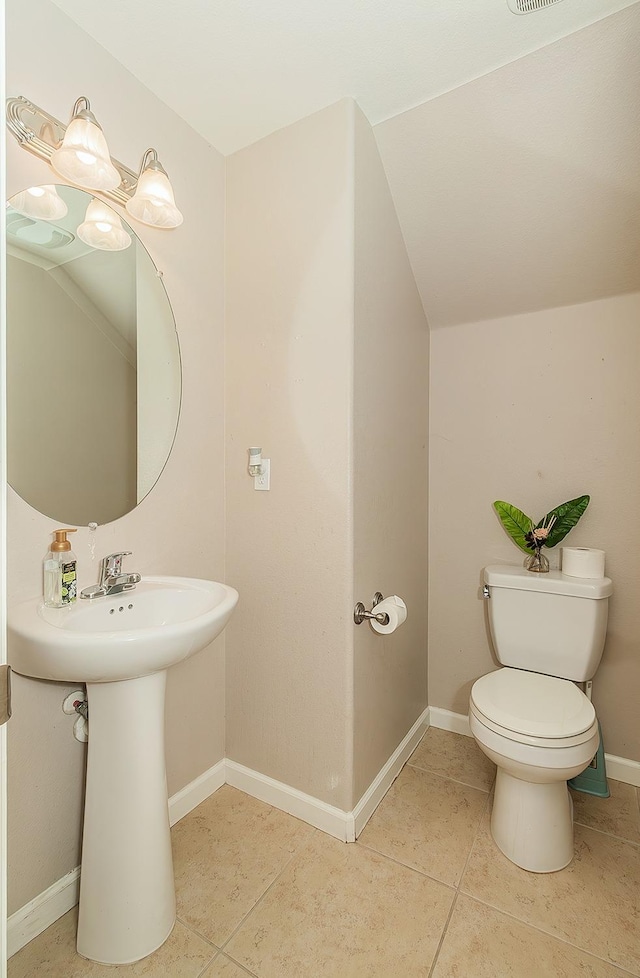 bathroom with lofted ceiling, toilet, a sink, tile patterned flooring, and baseboards