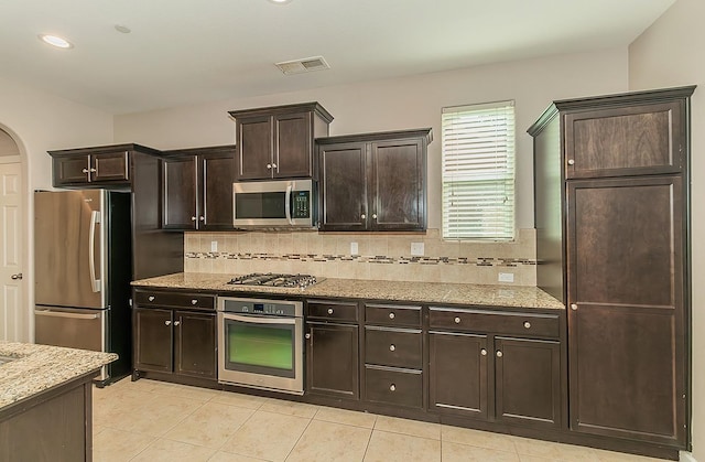 kitchen featuring visible vents, appliances with stainless steel finishes, arched walkways, and light stone counters