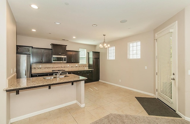 kitchen with a breakfast bar, decorative backsplash, appliances with stainless steel finishes, a sink, and light stone countertops