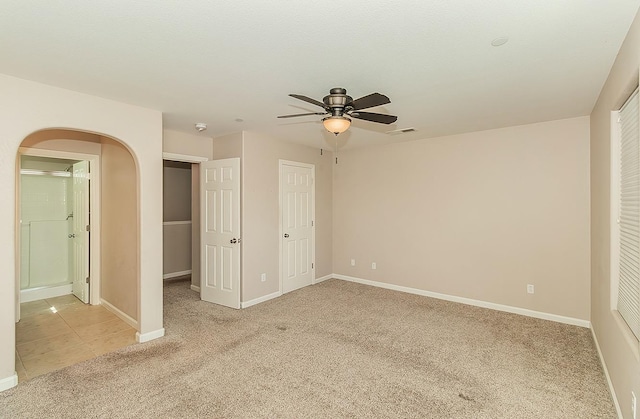 unfurnished bedroom featuring arched walkways, light colored carpet, visible vents, a ceiling fan, and baseboards