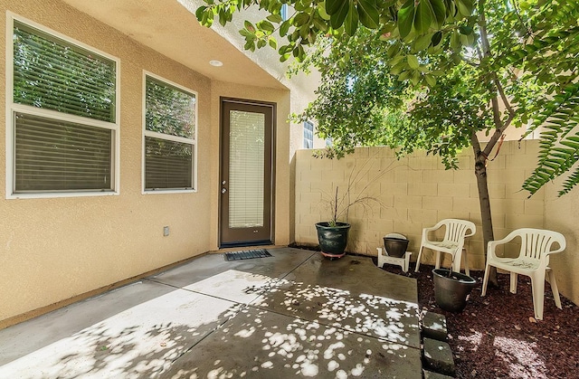 view of exterior entry featuring stucco siding, fence, and a patio