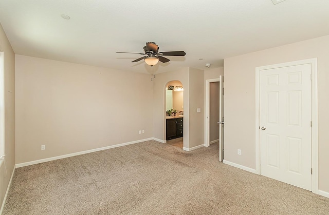 unfurnished bedroom with light carpet, baseboards, arched walkways, and ensuite bathroom