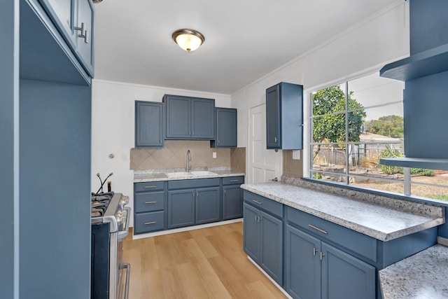 kitchen with light hardwood / wood-style floors, stainless steel range with gas cooktop, tasteful backsplash, blue cabinets, and sink