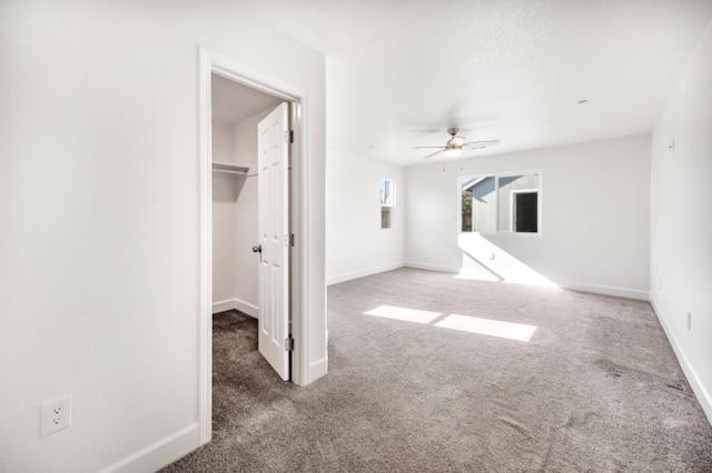 interior space with ceiling fan, a walk in closet, and dark carpet