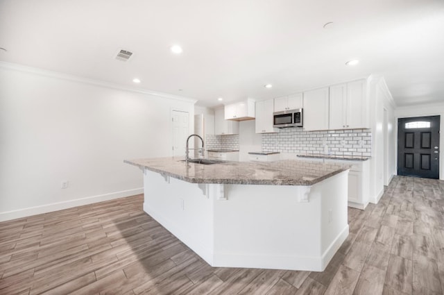 kitchen featuring light stone countertops, white cabinetry, sink, a kitchen breakfast bar, and a center island with sink