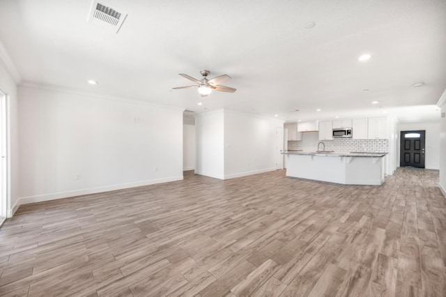 unfurnished living room featuring ceiling fan, light wood-type flooring, sink, and crown molding