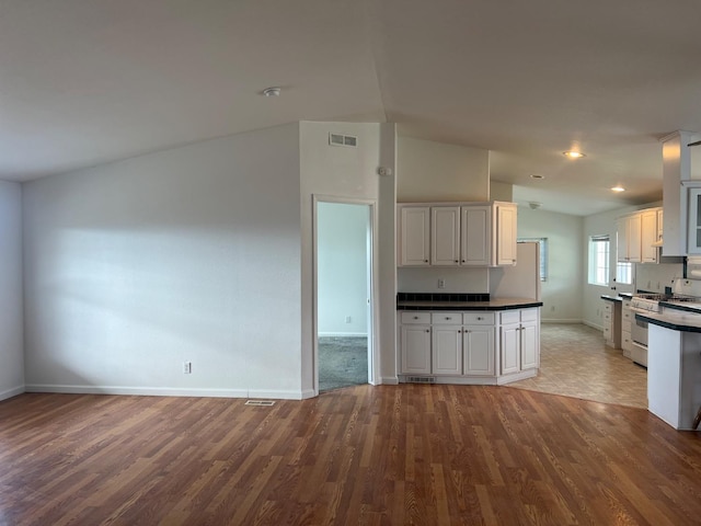 kitchen featuring white gas stove, vaulted ceiling, dark countertops, and wood finished floors
