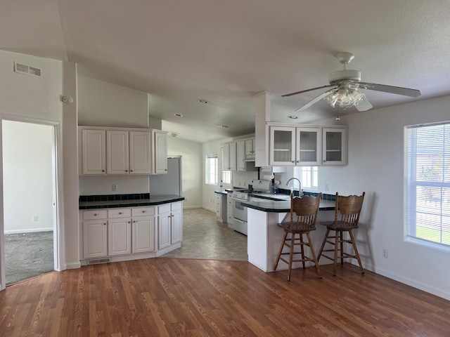 kitchen featuring visible vents, a peninsula, white range with gas stovetop, white cabinets, and a kitchen breakfast bar