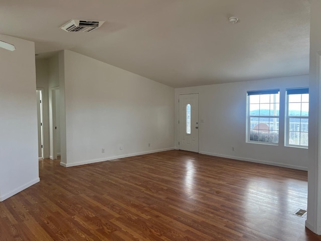 interior space with vaulted ceiling, dark wood-type flooring, visible vents, and baseboards