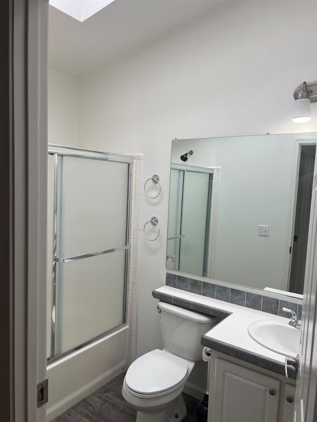 bathroom featuring a skylight, toilet, shower / bath combination with glass door, wood finished floors, and vanity