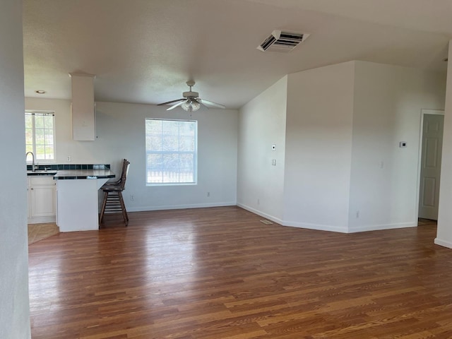 unfurnished living room featuring visible vents, baseboards, dark wood finished floors, a ceiling fan, and a sink