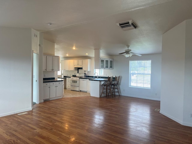 kitchen with white appliances, visible vents, baseboards, dark countertops, and light wood-style flooring