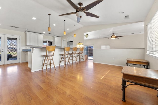 kitchen featuring decorative light fixtures, lofted ceiling, light wood-type flooring, white cabinets, and stainless steel fridge