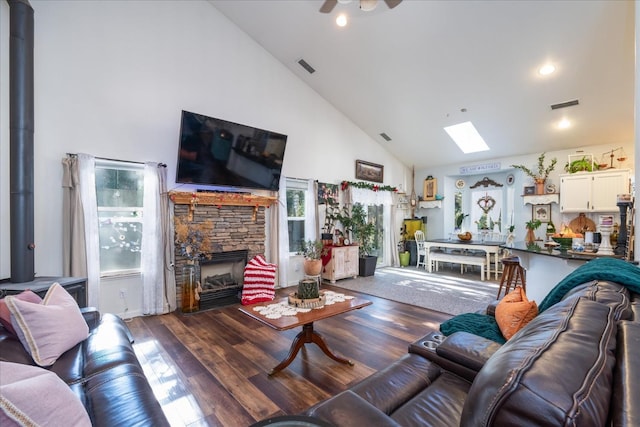 living room featuring ceiling fan, a skylight, a stone fireplace, high vaulted ceiling, and dark hardwood / wood-style flooring