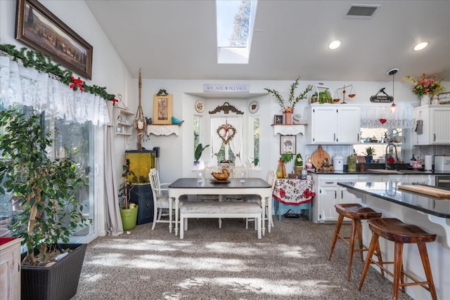 kitchen featuring carpet floors, white cabinetry, a healthy amount of sunlight, and hanging light fixtures