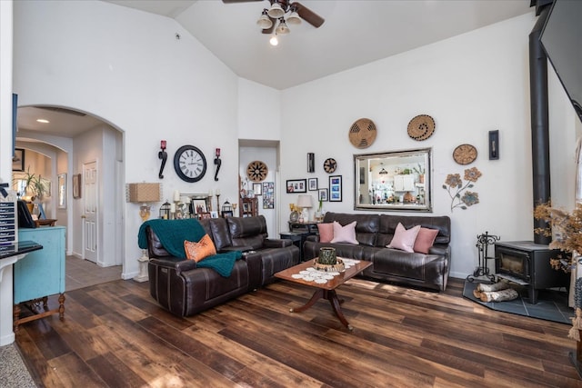 living room with ceiling fan, a wood stove, dark hardwood / wood-style floors, and high vaulted ceiling