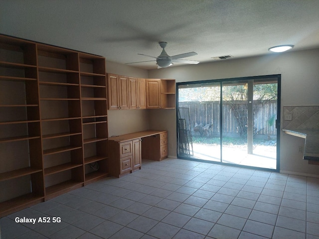 unfurnished office with ceiling fan, light tile patterned floors, and built in desk