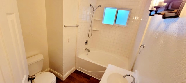 bathroom featuring hardwood / wood-style flooring, tiled shower / bath combo, and toilet