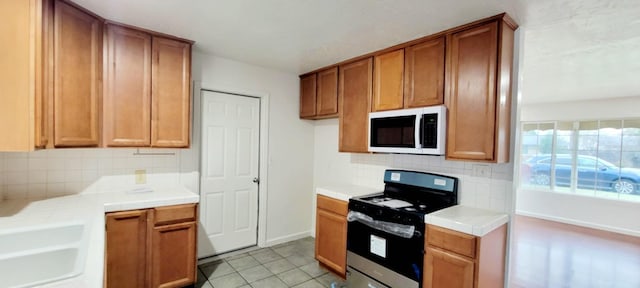 kitchen with tasteful backsplash, sink, electric range, and light tile patterned flooring