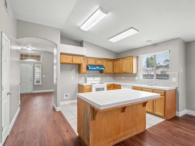 kitchen featuring tile countertops, lofted ceiling, a kitchen island, white appliances, and a kitchen bar