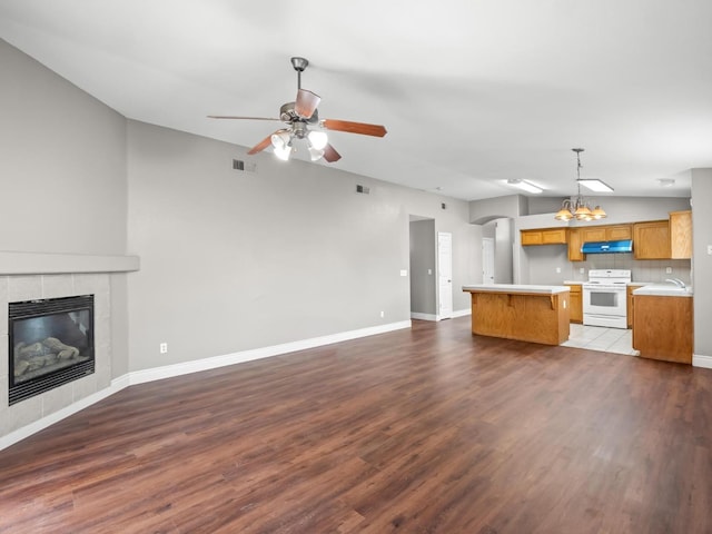 unfurnished living room with a tile fireplace, vaulted ceiling, dark wood-type flooring, and ceiling fan with notable chandelier