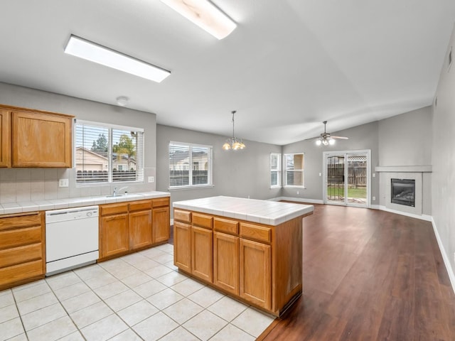 kitchen with tile countertops, dishwasher, a tiled fireplace, pendant lighting, and sink