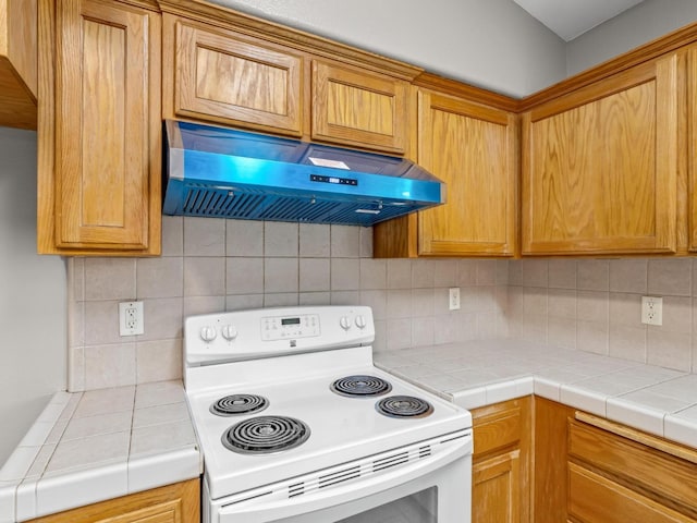 kitchen featuring electric stove, range hood, tile countertops, and backsplash