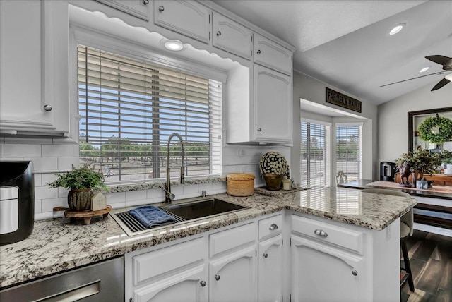 kitchen featuring white cabinetry, backsplash, lofted ceiling, stainless steel dishwasher, and sink