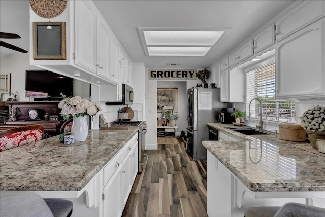 kitchen featuring white cabinetry, a kitchen bar, appliances with stainless steel finishes, dark wood-type flooring, and sink