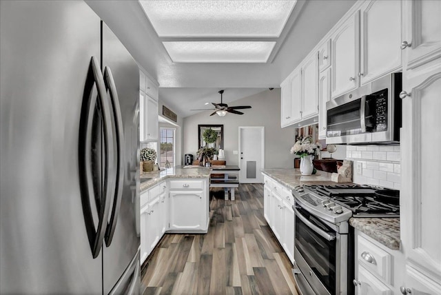 kitchen featuring appliances with stainless steel finishes, lofted ceiling, white cabinetry, backsplash, and light stone counters