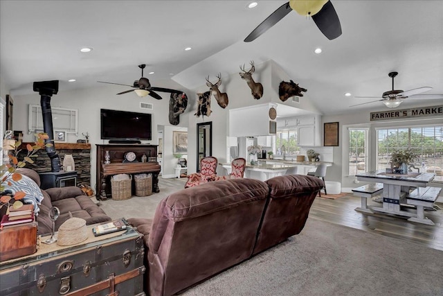 living room featuring sink, lofted ceiling, a wood stove, and light hardwood / wood-style floors