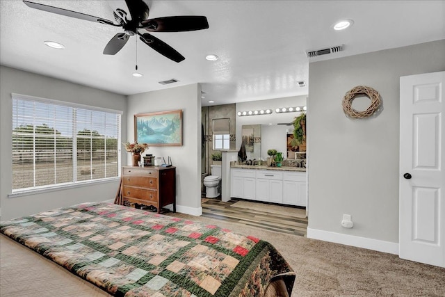 bedroom featuring ceiling fan, ensuite bathroom, and light colored carpet