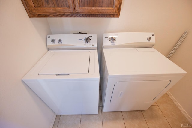 washroom featuring light tile patterned floors, washer and clothes dryer, cabinet space, and baseboards