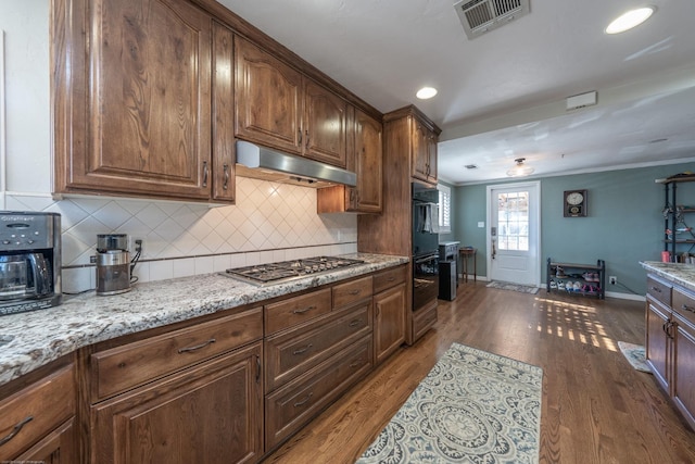 kitchen featuring dark wood-style flooring, visible vents, dobule oven black, light stone countertops, and under cabinet range hood