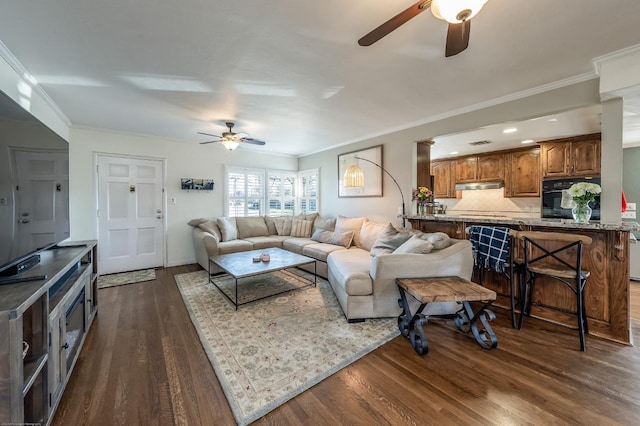 living area featuring ceiling fan, dark wood-type flooring, and crown molding