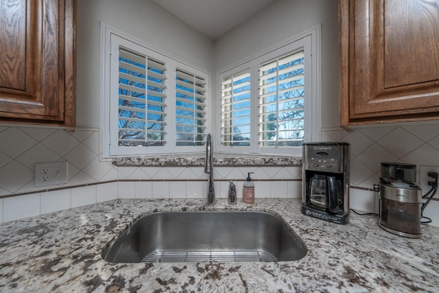 kitchen with brown cabinets, light stone countertops, decorative backsplash, and a sink