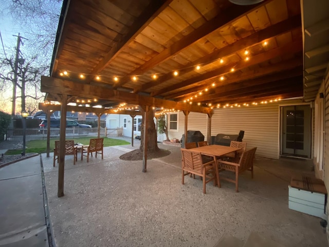 patio terrace at dusk featuring grilling area, fence, and outdoor dining area