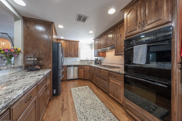 kitchen with light stone counters, under cabinet range hood, a sink, visible vents, and appliances with stainless steel finishes