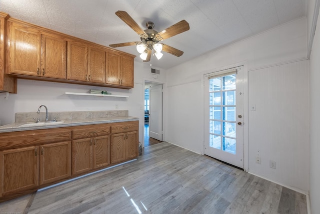 kitchen featuring light wood finished floors, open shelves, light countertops, brown cabinetry, and a sink