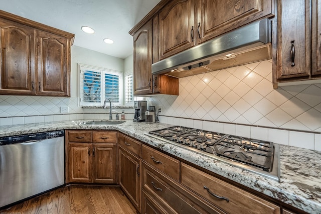 kitchen with stainless steel appliances, a sink, under cabinet range hood, and light stone countertops