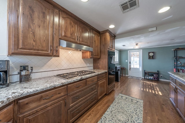 kitchen featuring under cabinet range hood, dark wood-type flooring, visible vents, tasteful backsplash, and stainless steel gas stovetop