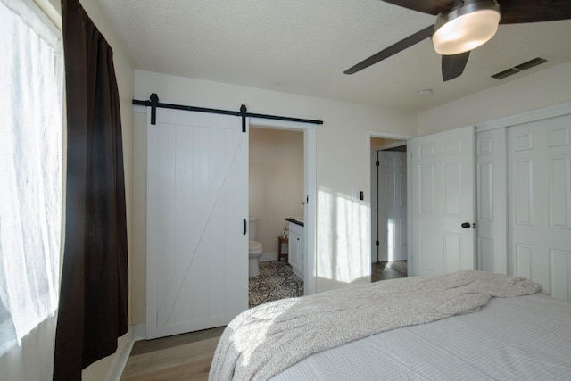 bedroom with a barn door, light hardwood / wood-style floors, ceiling fan, connected bathroom, and a closet