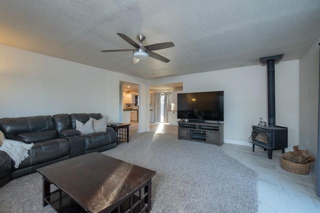 living room with ceiling fan, a wood stove, and a textured ceiling