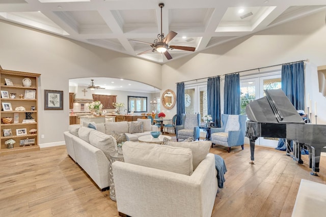 living room featuring ceiling fan, light hardwood / wood-style flooring, a high ceiling, and coffered ceiling