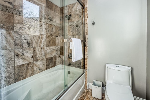 bathroom with toilet and shower / bath combination with glass door