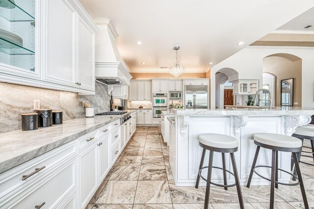 kitchen featuring white cabinetry, tasteful backsplash, hanging light fixtures, built in appliances, and a breakfast bar