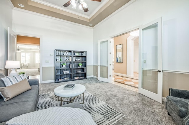 carpeted living room featuring ceiling fan, a tray ceiling, ornamental molding, and french doors