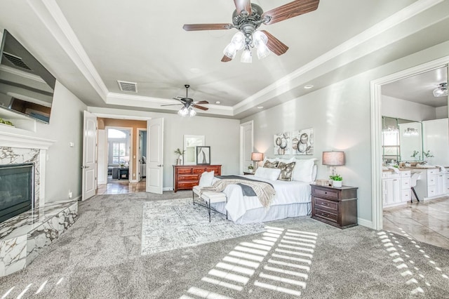 bedroom with light carpet, ceiling fan, a premium fireplace, and a tray ceiling