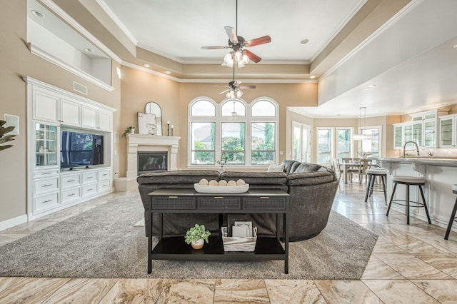 living room featuring a high ceiling, sink, a raised ceiling, ceiling fan, and crown molding